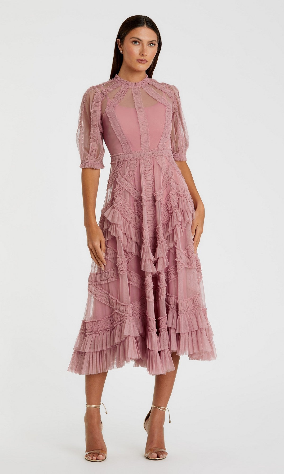 A woman in the Mac Duggal 8058 Ruffled Midi Wedding-Guest Dress in Antique Rose, featuring ruffled and sheer accents, stands in strappy high-heeled sandals against a plain light background.